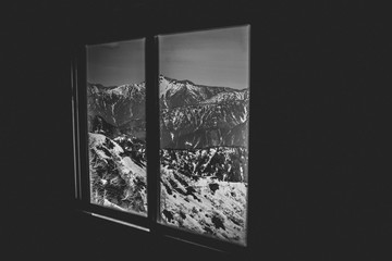The ice-covered mountains in the late winter are seen from the window in a dark room.