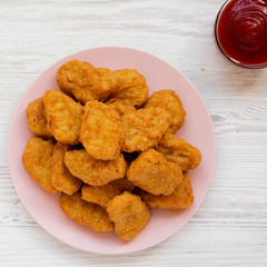 Chicken nuggets on a pink plate, ketchup on a white wooden surface, top view. Overhead, from above, flat lay. Copy space.