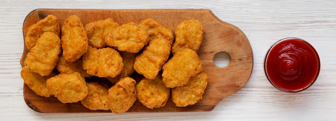 Chicken nuggets on a rustic wooden board on a white wooden surface, top view. Flat lay, from above, overhead.