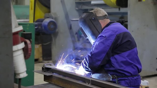A worker in a mask welds between metal parts