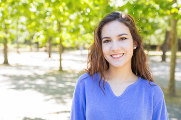 Fototapeta premium Cheerful young woman with wavy hair walking in summer park. Portrait of beautiful woman in blue sweater. Stroll concept