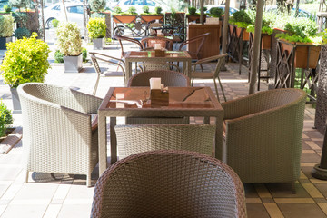 tables and wicker chairs in outdoor summer cafe with flower beds