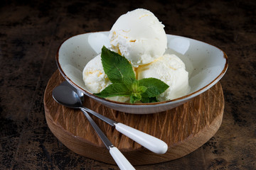 Vanilla ice cream in a plate on a dark wooden background. Horizontal photo.