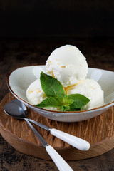 Vanilla ice cream in a plate on a dark wooden background. Vertical photo.