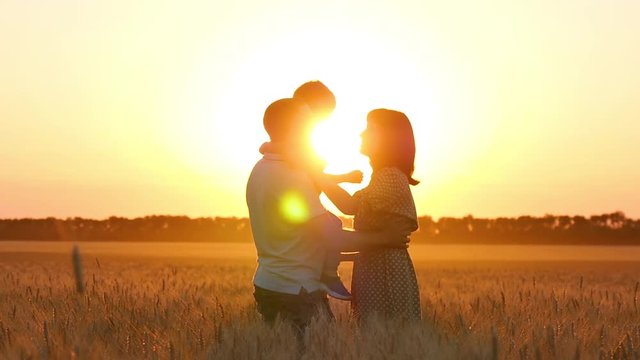 Happy family in a wheat field in the sun at sunset. The father holds the child in his arms. A woman kisses her man and child.