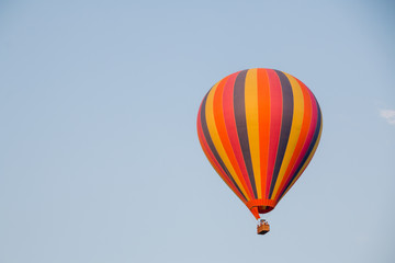 Colorful hot air balloon moving up in blue sky.