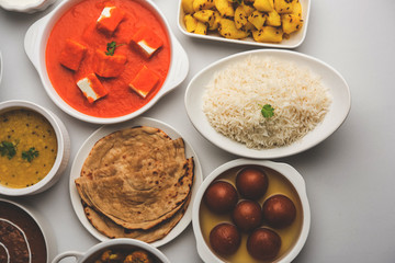 Assorted Indian food like paneer butter masala, dal, roti, rice, sabji, gulab jamun and bound raita served in bowls over moody background, selective focus - obrazy, fototapety, plakaty