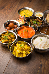 Assorted Indian food like paneer butter masala, dal, roti, rice, sabji, gulab jamun and bound raita served in bowls over moody background, selective focus