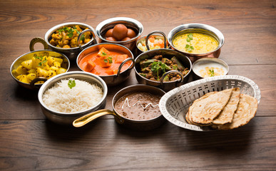 Assorted Indian food like paneer butter masala, dal, roti, rice, sabji, gulab jamun and bound raita served in bowls over moody background, selective focus - obrazy, fototapety, plakaty