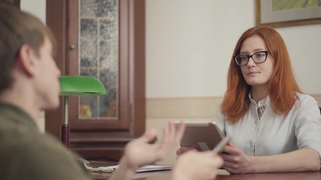 Portrait of cute young woman psychotherapist having session with her patient. Beautiful red-haired woman psychologist with glasses and tablet. Guy shares his problems and fears. Mental health.