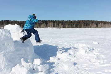 Boy jumping from an unfinished igloo in the snow in winter