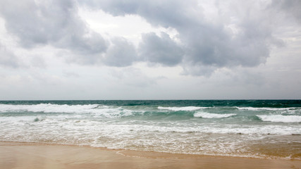 Sunset on Karon beach. Heavy clouds over the sea. The surf pounds the shore. Phuket, Thailand