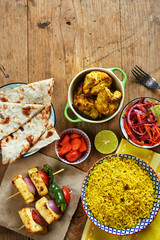 Top view of basmati rice, naan bread, grilled cheese, chicken kebab and pickled vegetables. Indian style lunch on wooden table with copy space.