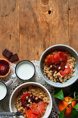 Two bowls of porridge with red oranges and chocolate and fresh milk over wooden table. Flat lay with space for text.