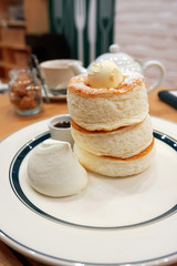 Close up of stack of fluffy pancakes with butter, cream and maple syrup on white plate in cafe in Japan. 