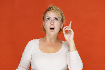 Fototapeta premium Photo portrait of a beautiful girl blonde woman with short curly hair on a red background talking and showing a lot of emotions. An experienced model shows hands. Beauty. Made in studio