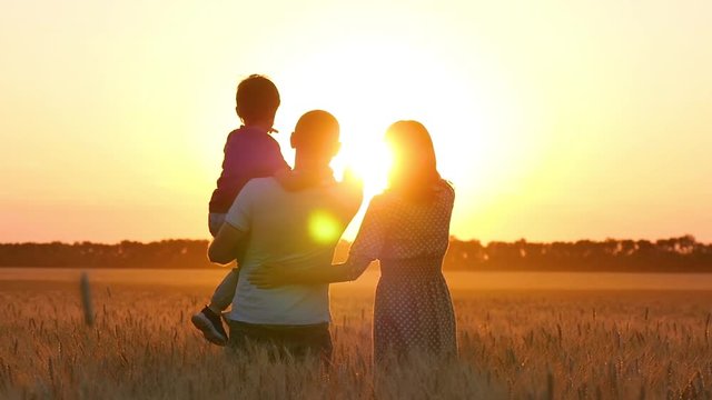 Father and mother point the child to the horizon in a wheat field. Happy family at sunset. Agriculture, relationships.