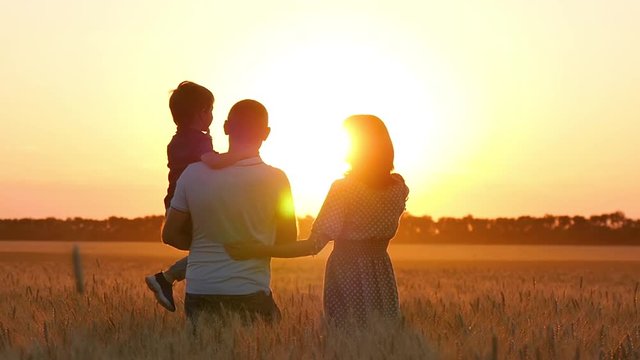 Mom, dad and baby hug and kiss each other standing in a wheat field at sunset. The concept of a happy family, care and relationships.
