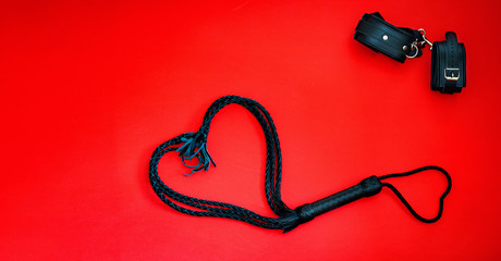 Accessories for bdsm on a red leather background. Lash in the shape of a heart and leather...