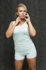 Fototapeta premium Photo portrait above the knee of a beautiful girl blonde woman with short curly hair on a gray background in bright linen is talking and showing a lot of emotions. An experienced model shows hands.