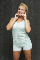 Photo portrait above the knee of a beautiful girl blonde woman with short curly hair on a gray background in bright linen is talking and showing a lot of emotions. An experienced model shows hands.
