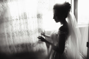 Beautiful bride style. Wedding girl stand in luxury wedding dress near window. Black and white