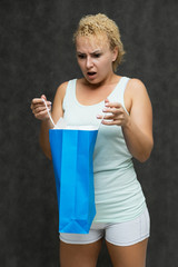 a portrait above the knee of a beautiful blonde woman girl with short curly hair on a gray background in light-colored underwear with packages from a gift shop and shows a lot of emotions.