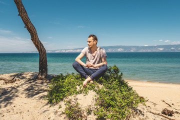 Fototapeta na wymiar Man traveler relaxing on the beach of Olkhon island overlooking the water of the lake and the mountains and the blue sky