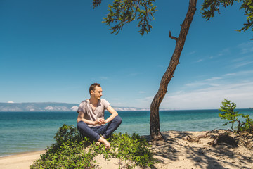 Man traveler relaxing on the beach of Olkhon island overlooking the water of the lake and the mountains and the blue sky