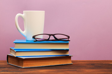  pile of old books with mug ang glasses  panorma, good copy space  on pink background