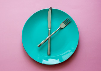 Clean green plate and stainless knife and fork isolated on pink background. Time to eat