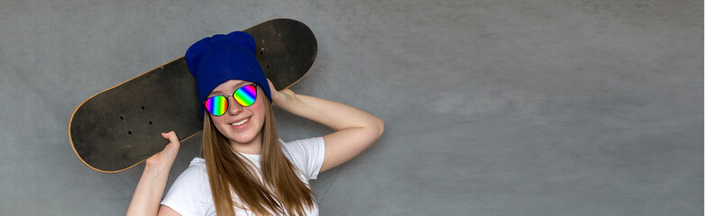 Teenager girl in sunglasses and hipster millennial hat with skateboard near the colorful wall,...