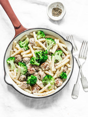 Creamy meatballs, broccoli pasta in a frying pan on a light background, top view