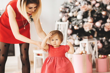 Happy mother with her daughter, red dresses near the Christmas tree at home. Christmas decorated interior