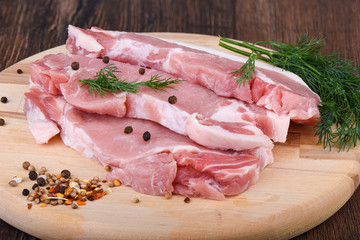 Pork steaks on a wooden cutting board with dill and spices. Raw pork meat for steaks.