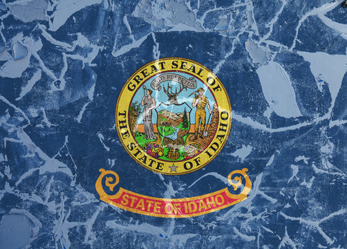 The national flag of the US state Idaho in against a gray wall with cracks and faults on the day of independence in color of blue red and yellow. Political and religious disputes, customs and delivery