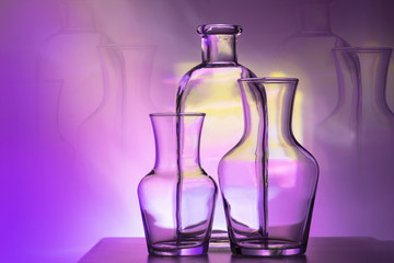 The outline of two glass vases and bottles on a bright purple and yellow colored background, horizontal layout.