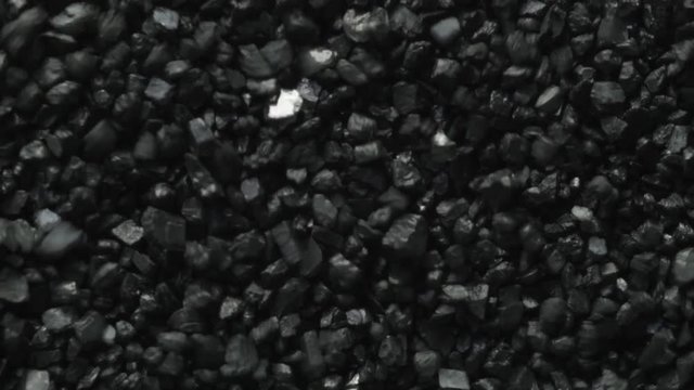 Macro shot of black coal stones shaking and moving forward through vibrations of sound.