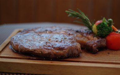 Grilled steak with black pepper, small tomatos, rosemary, broccoli and asparagus on wood plate