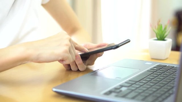 Asian business woman using smart phone while working on laptop