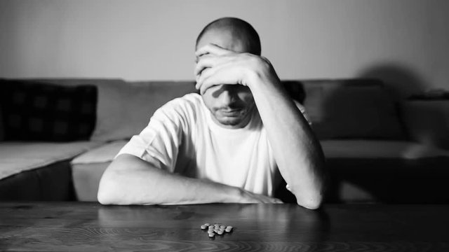 Depressed man suffering from suicidal depression want to commit suicide by overdose taking strong medicament drugs and pills pain killers sitting in his dark room selective focus moody dramatic look