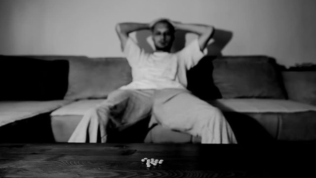 Depressed man suffering from suicidal depression want to commit suicide by overdose taking strong medicament drugs and pills pain killers sitting in his dark room selective focus moody dramatic look