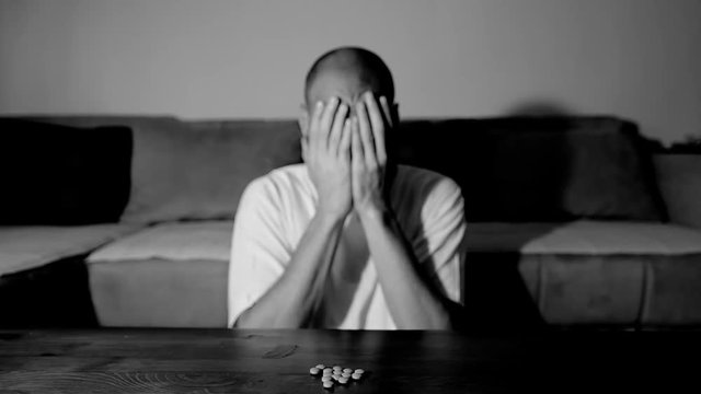 Depressed man suffering from suicidal depression want to commit suicide by overdose taking strong medicament drugs and pills pain killers sitting in his dark room selective focus moody dramatic look