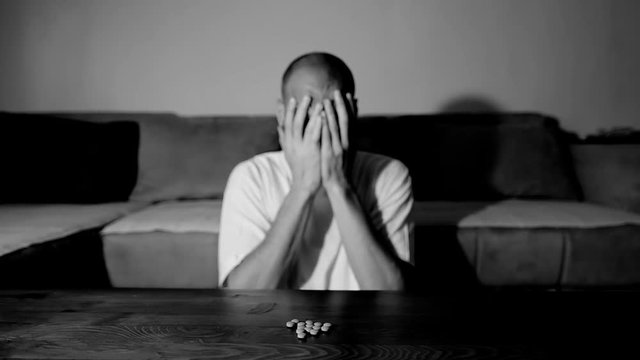 Depressed man suffering from suicidal depression want to commit suicide by overdose taking strong medicament drugs and pills pain killers sitting in his dark room selective focus moody dramatic look