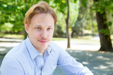 Joyful attractive guy posing in park. Closeup of young man looking at camera and smiling. Handsome man concept