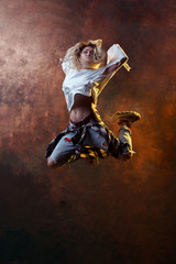 Naklejka na ściany i meble Photo of jumping blonde dancer girl looking back in torn jeans and sneakers on dark brown background