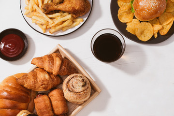 Freshly baked buns, big hamburger, fried crispy chicken and french fries on white table - Unhealthy food concept
