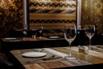 Empty wine glasses and tableware close up view on wooden table in restaurant with silk rugs on the wall