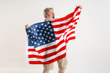 Celebrating an Independence day. Stars and Stripes. Senior man with the flag of the United States of America isolated on white studio background. Looks crazy happy and proud as a patriot of his