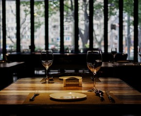 Empty wine glasses, knife and fork, white plate on wooden table in romantic restaurant